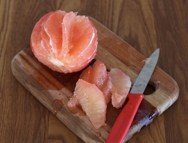 cutting sections of grapefruit on wooden board with red handled knife