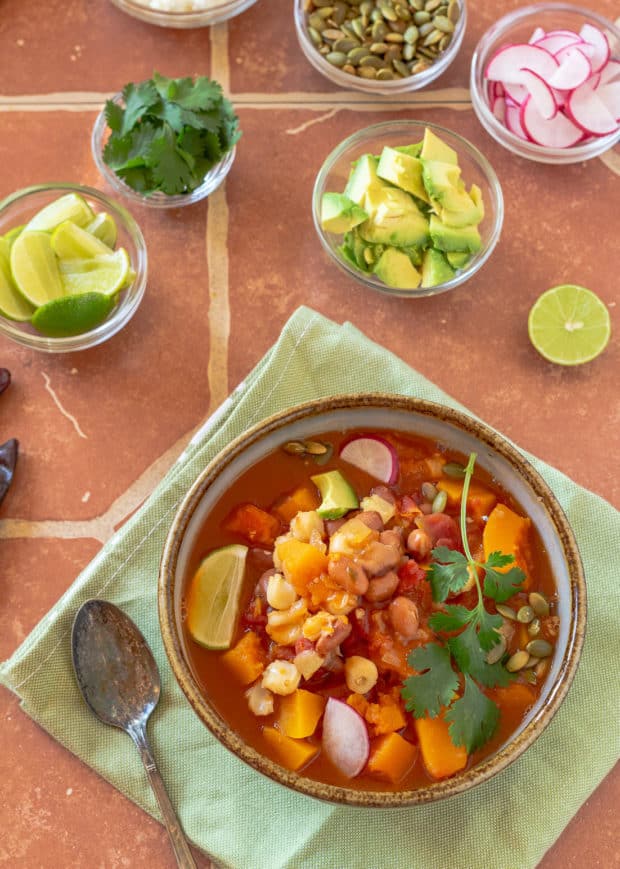 Butternut Squash Pozole in bowl ready to eat with avocado, cilantro, and lime wedge in separate bowls