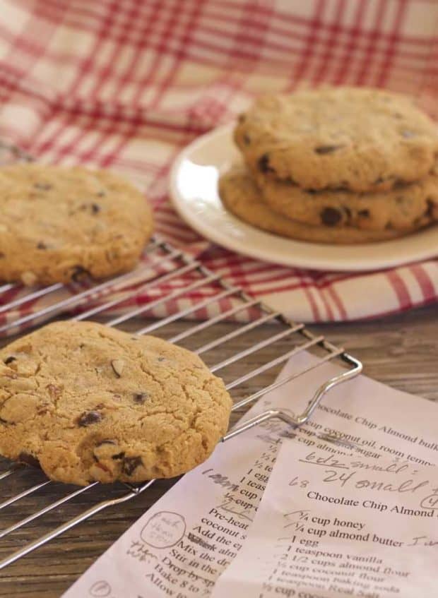 Jumbo Chocolate Chip Almond Cookies on cooling rack and on plate, with marked up recipe drafts