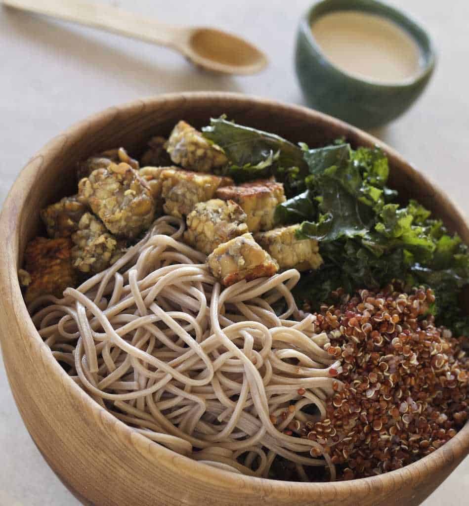 Soba Noodles, Kale, Tempeh and quinoa in a wooden bowl with Tahini Sauce on the side