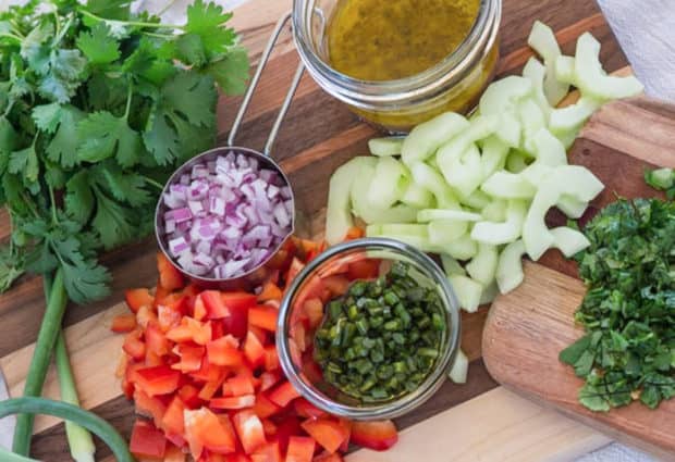 herbs and chopped veggies and dressing for salad scattered on wooden board