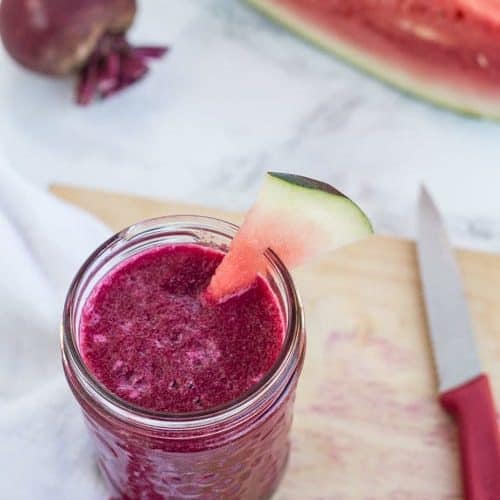 watermelon and beet smoothie in jar with watermelon wedge. Beet and watermelon in background.