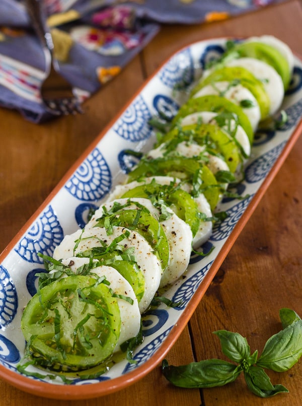 Green Zebra Tomatoes alternating with slices of fresh mozzarella on blue print platter