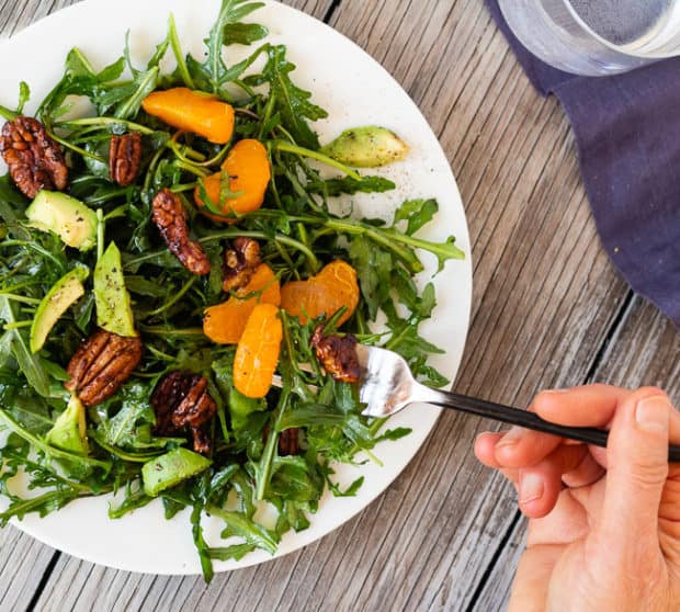Arugula Salad with Clementines and Maple Pepper Pecans with hand and fork
