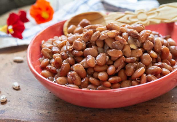  cooked pinto beans in a pretty bowl with wooden spoon