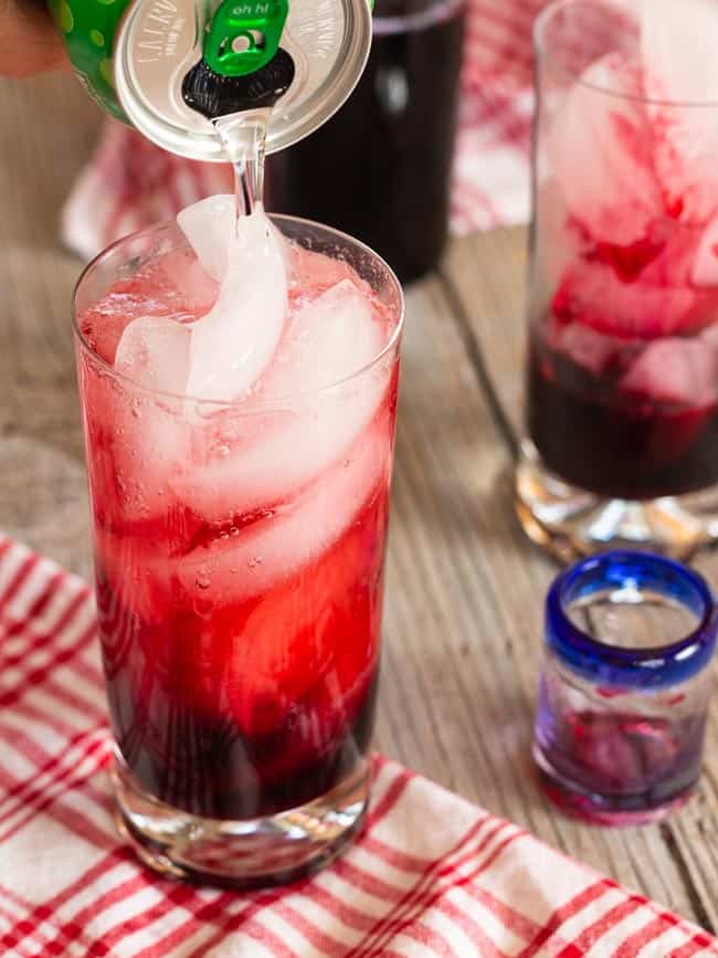pouring sparkling water into glass of ice and hibiscus syrup