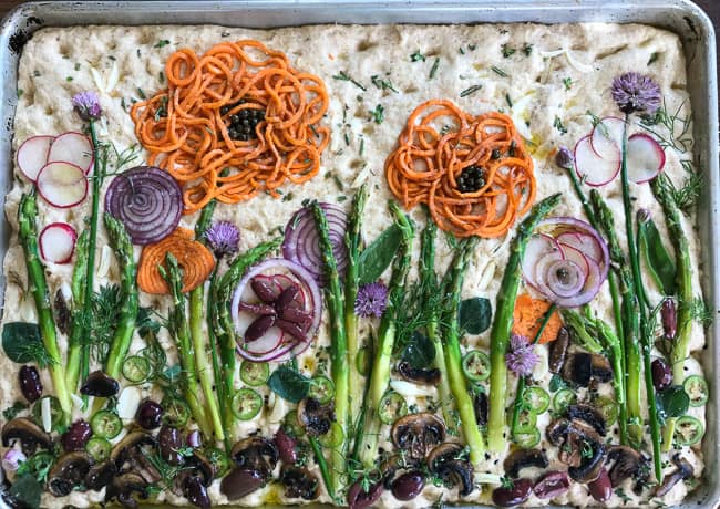 unbaked focaccia with vegetables and herbs on top to make a fanciful garden