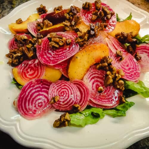 chiogga beets and peaches and candied pecans with arugula, on a white plate