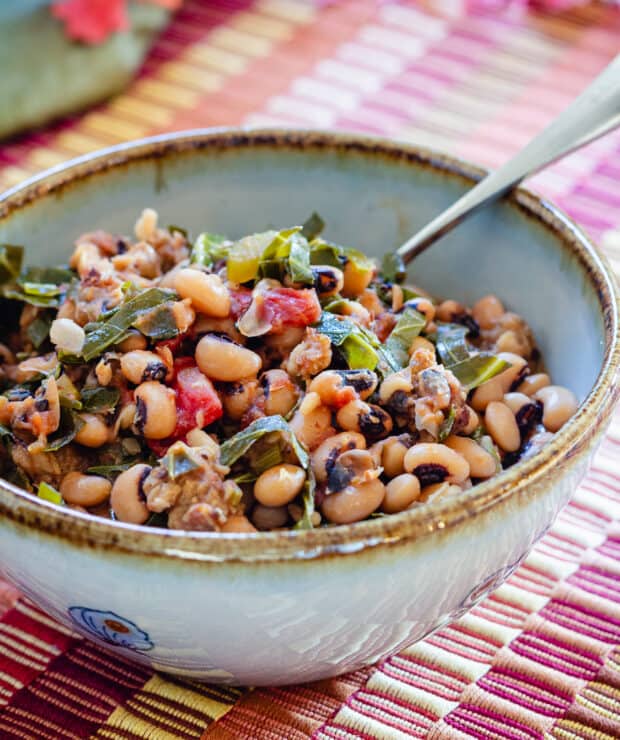 Black eyed peas and collard greens in blue bowl with brown rim and spoon